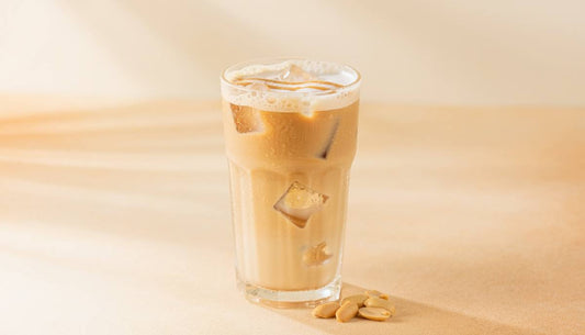 Iced peanut butter protein latte in a tall glass with ice and peanuts
