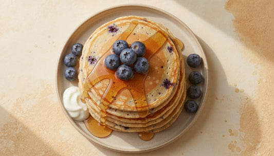Stack of blueberry protein pancakes topped with fresh blueberries and maple syrup