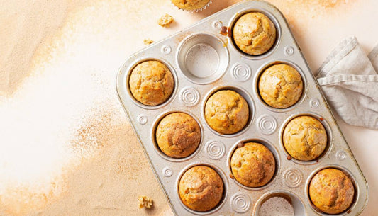 Overhead of golden-brown protein pumpkin muffins in a muffin tin on a warm cream surface